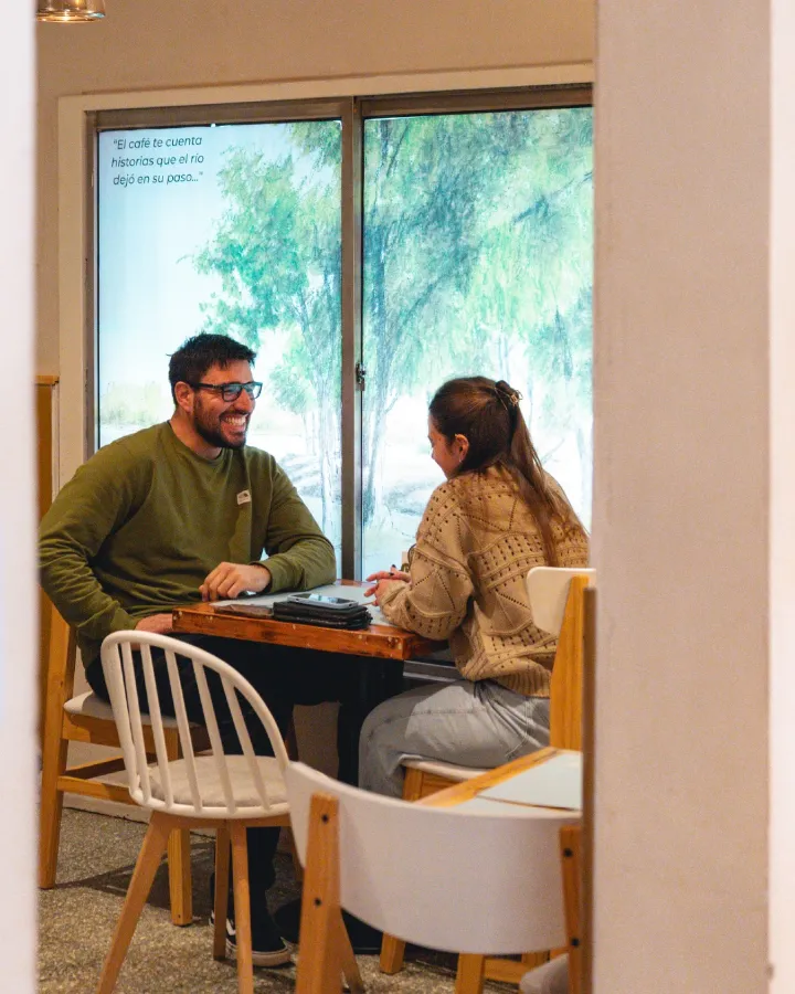 Dos personas charlando en una mesa junto a la ventana