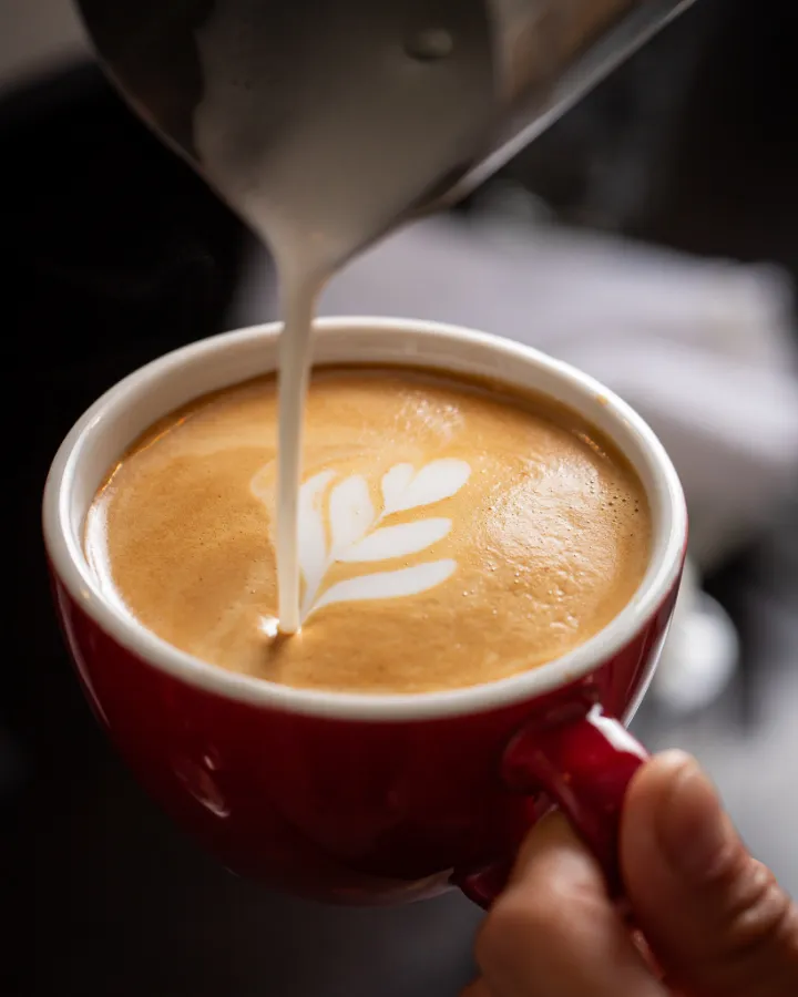 Leche vaporizada cayendo en una taza roja para hacer latte art