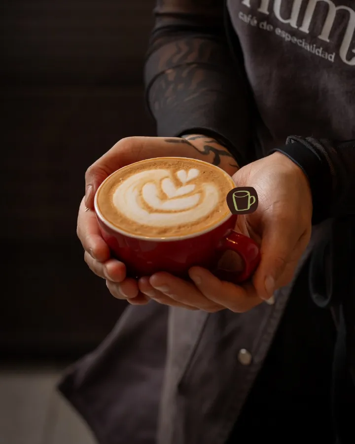 Manos sosteniendo una taza roja con latte art